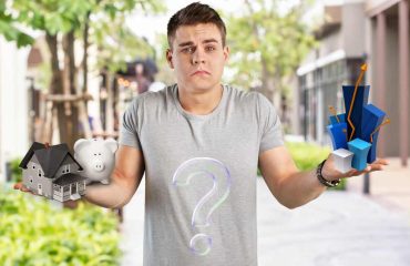 Man in a grey t-shirt showing confusion about a house and savings decision in one hand and an investment opportunity in the other. Standing in a leafy green street.